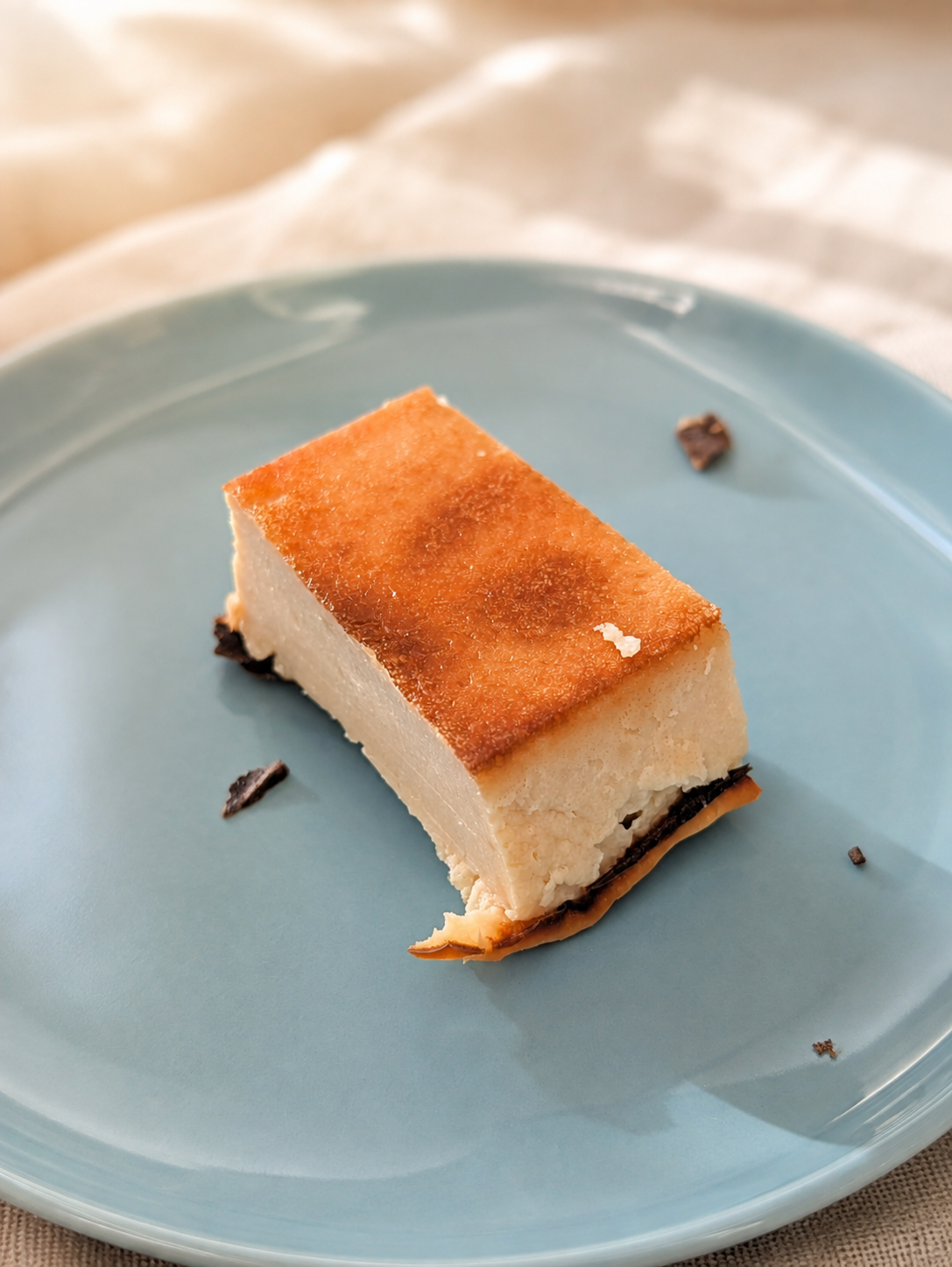 水色の皿にのせた、表面に焼き色のついた四角いヨーグルトケーキ
