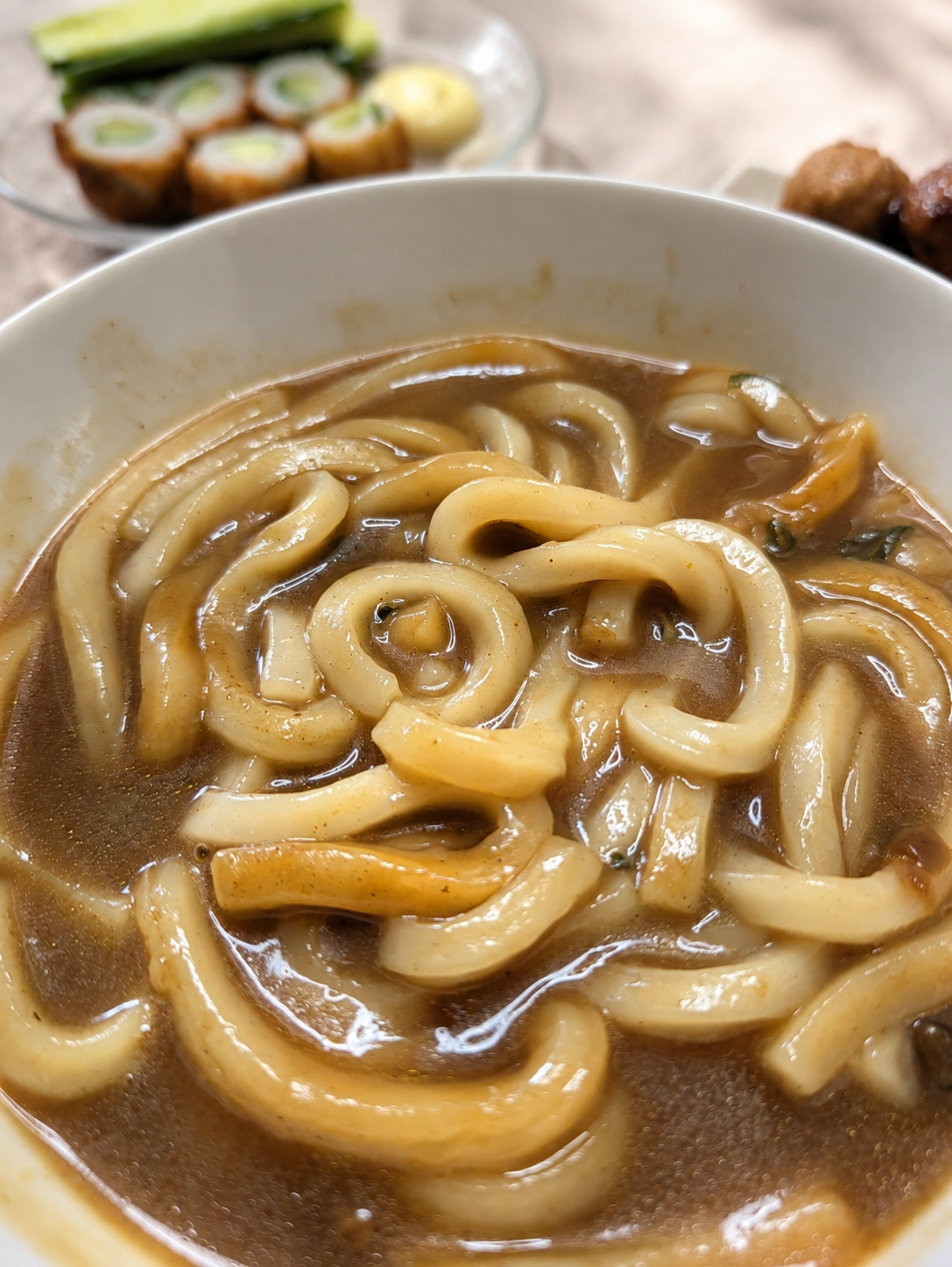 白い丼になみなみと入ったカレーうどん。奥にちくわのキュウリ詰めとマヨネーズ、肉団子