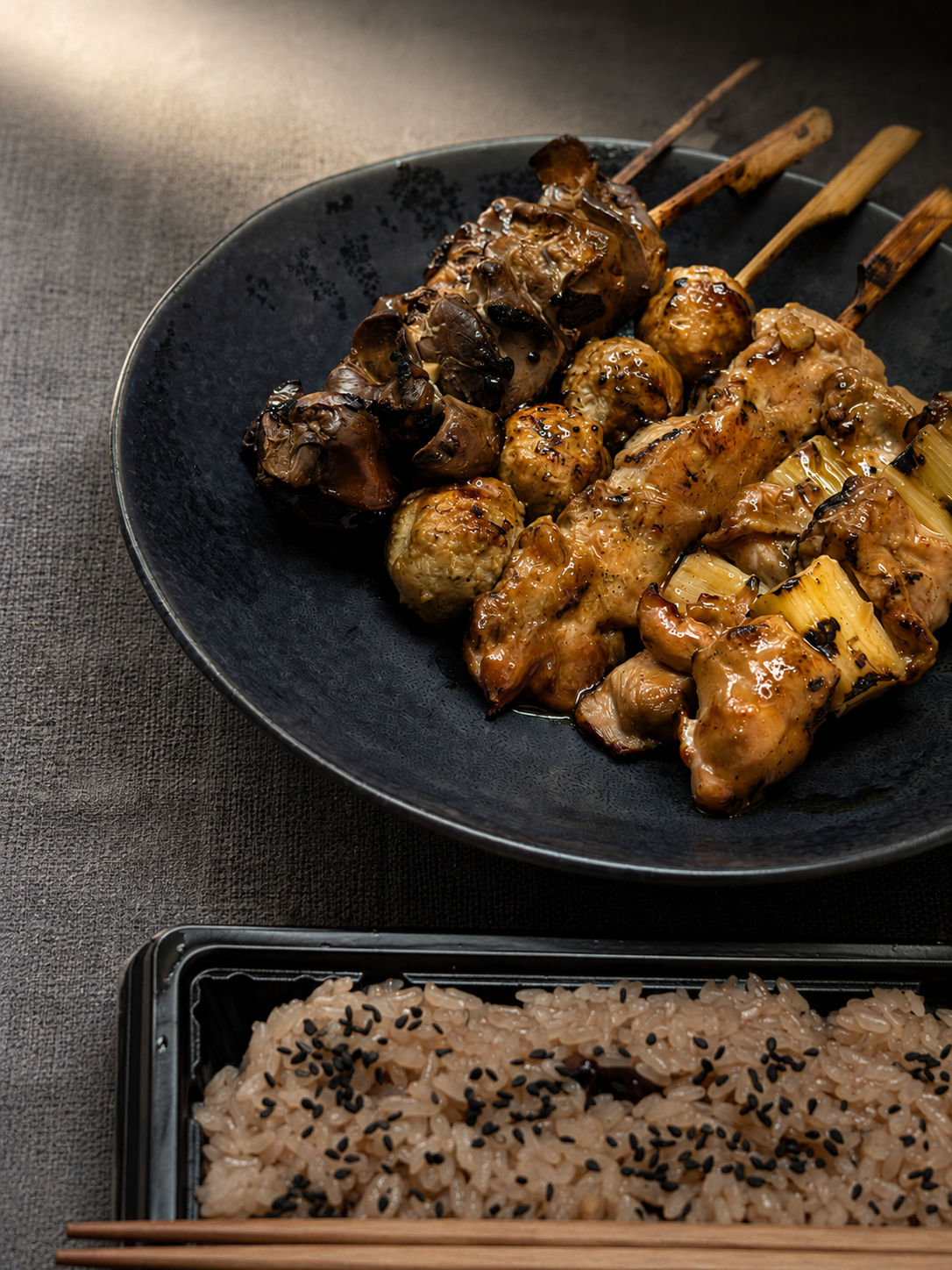 黒い皿に盛られたやきとり串と、黒ごまをふった赤飯