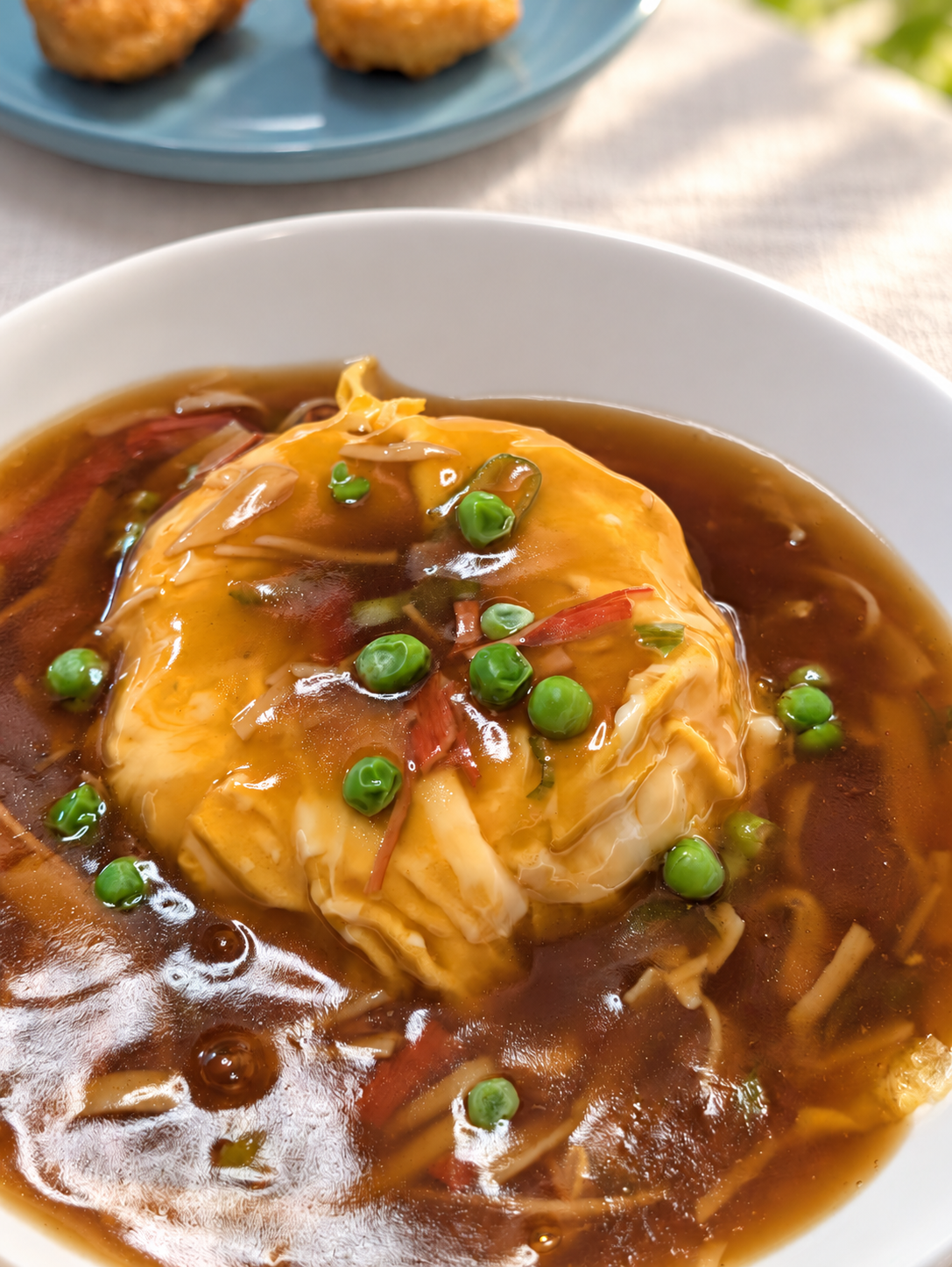 白い深皿に盛られた天津飯。グリンピースを散らしたあんがかかっている