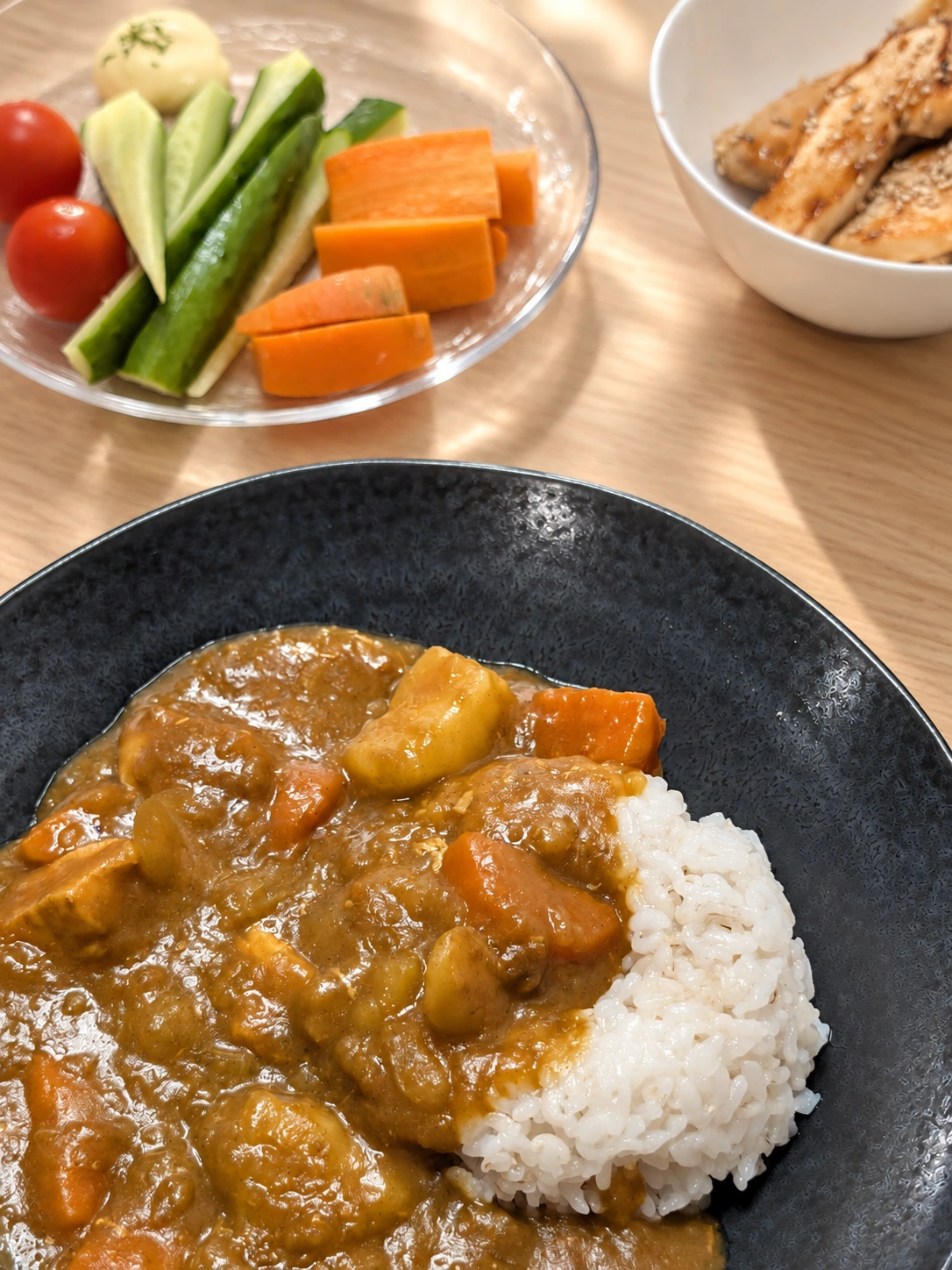 黒い皿に盛られたカレーライスと野菜スティック、照り焼きチキンの小鉢