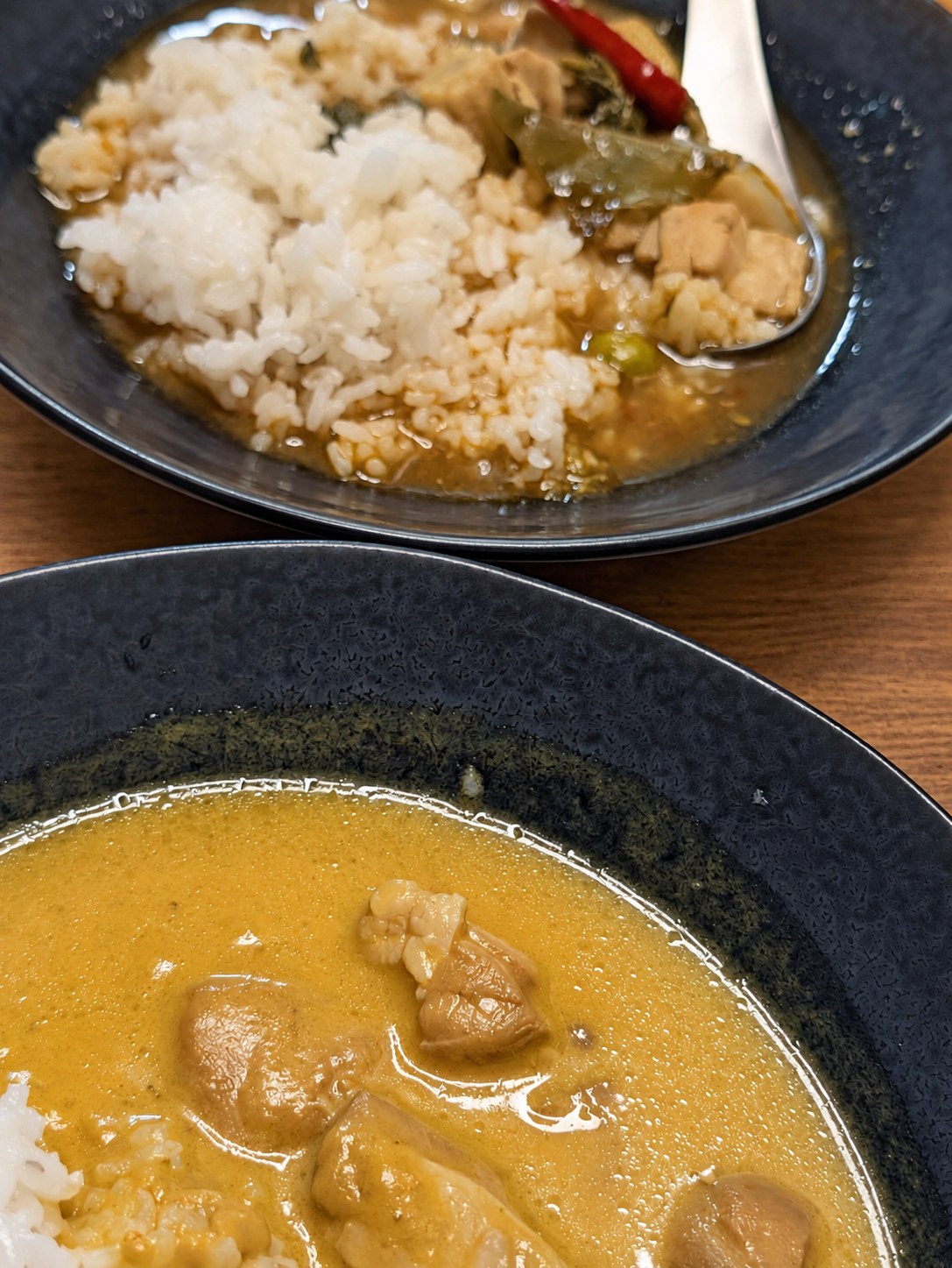 黒い深皿に盛ったタイカレー2種。手前は黄色いマンゴーカレー、奥はご飯にかけたゲーンパー