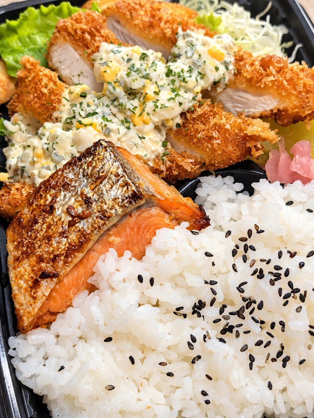 焼き鮭とタルタルソースのかかった揚げ物、ご飯が入った弁当(AIで光と色味を調整)