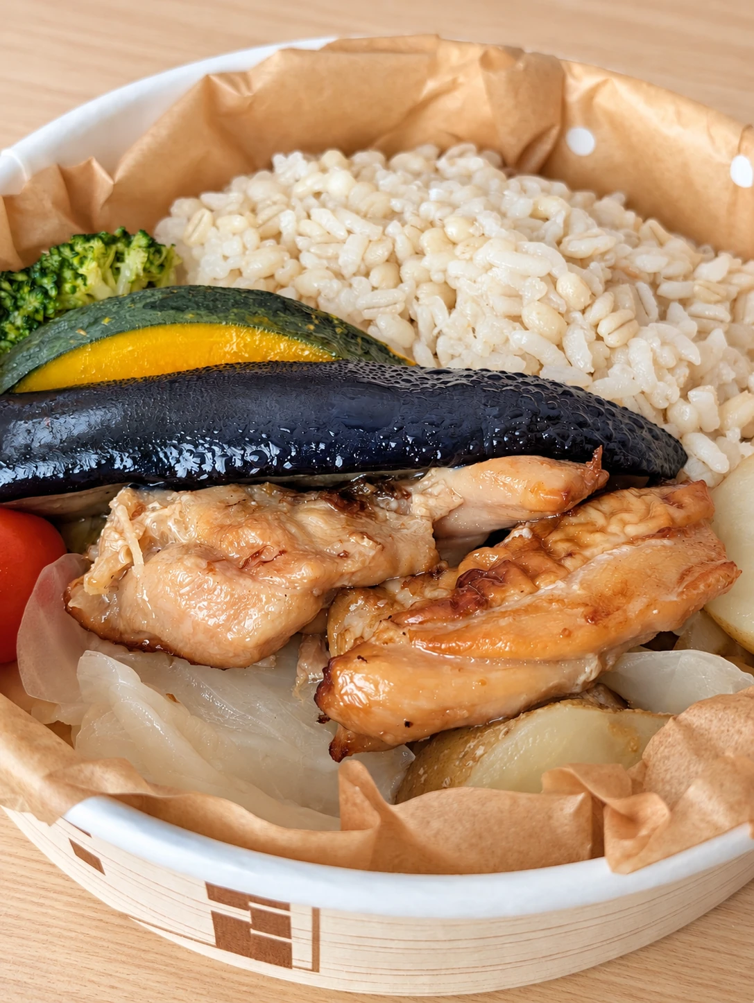ご飯と肉、かぼちゃ、なすなどが入った丸いお弁当(卓上と明るさはAIで加工)