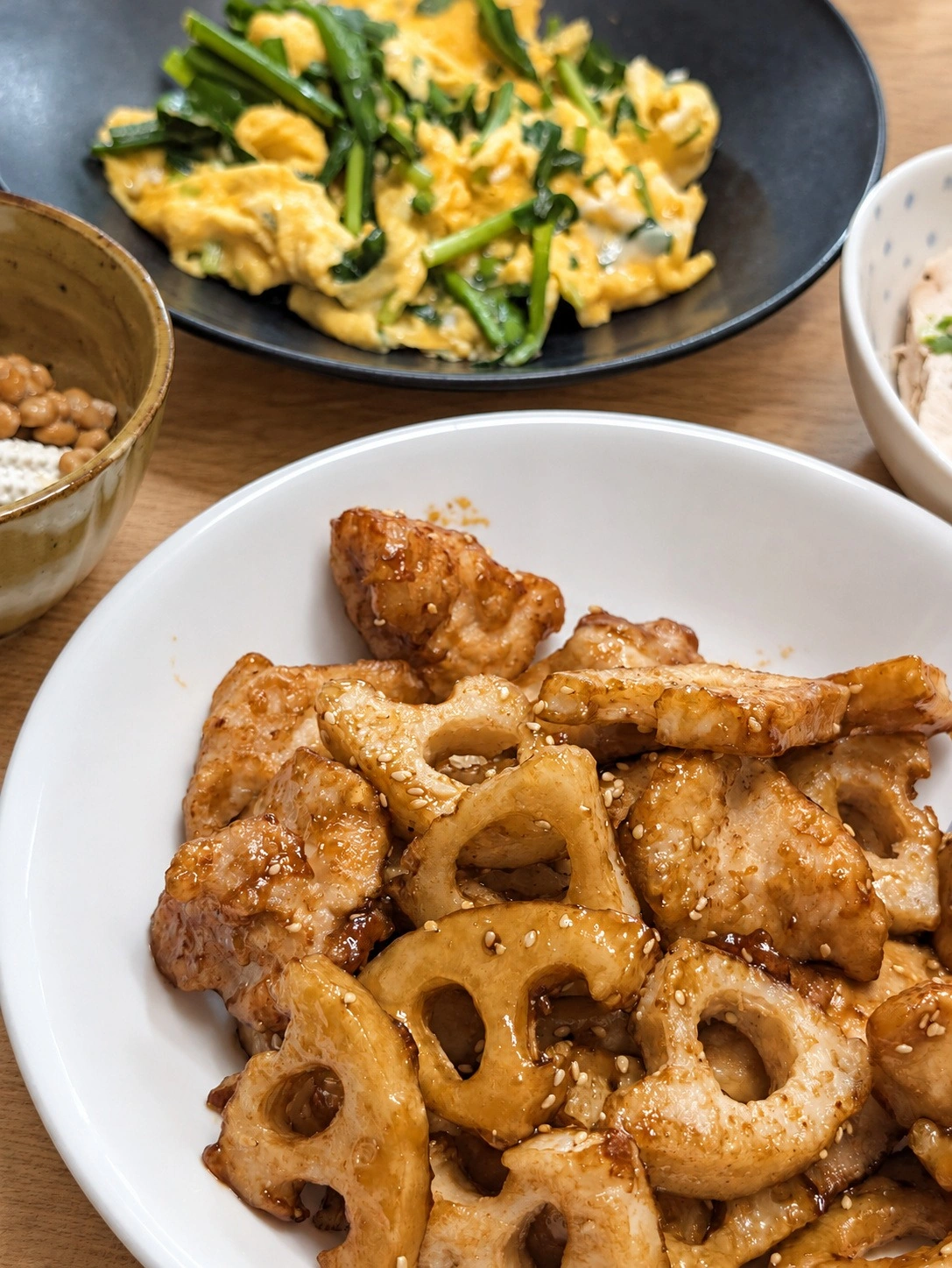 れんこんと鶏肉の炒め物、ニラ玉、納豆、冷ややっこが並ぶ夕食（卓上と明るさはAIで加工）