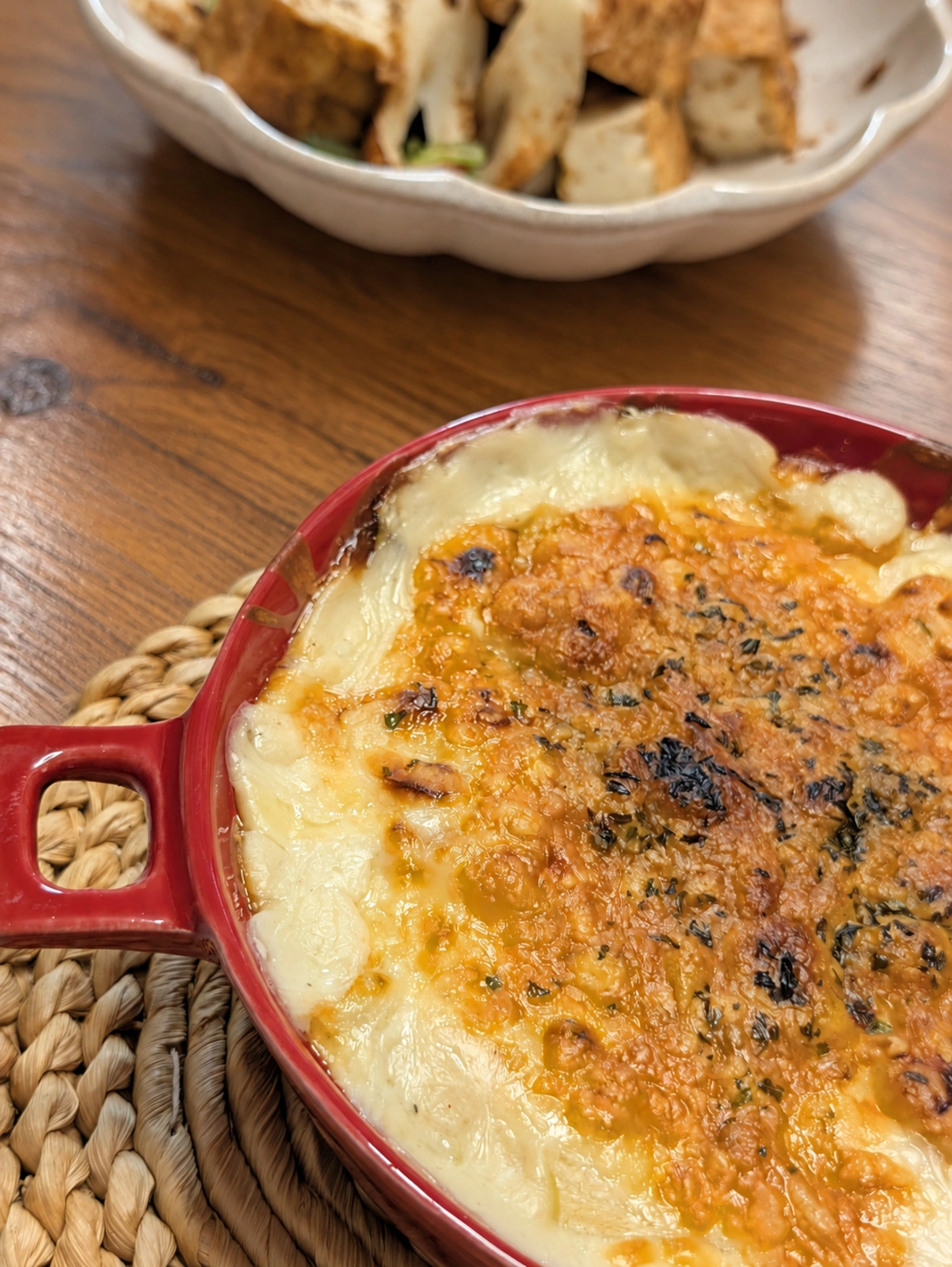 夕食のドリア。赤い耐熱皿と奥の小鉢（卓上はAIで加工）