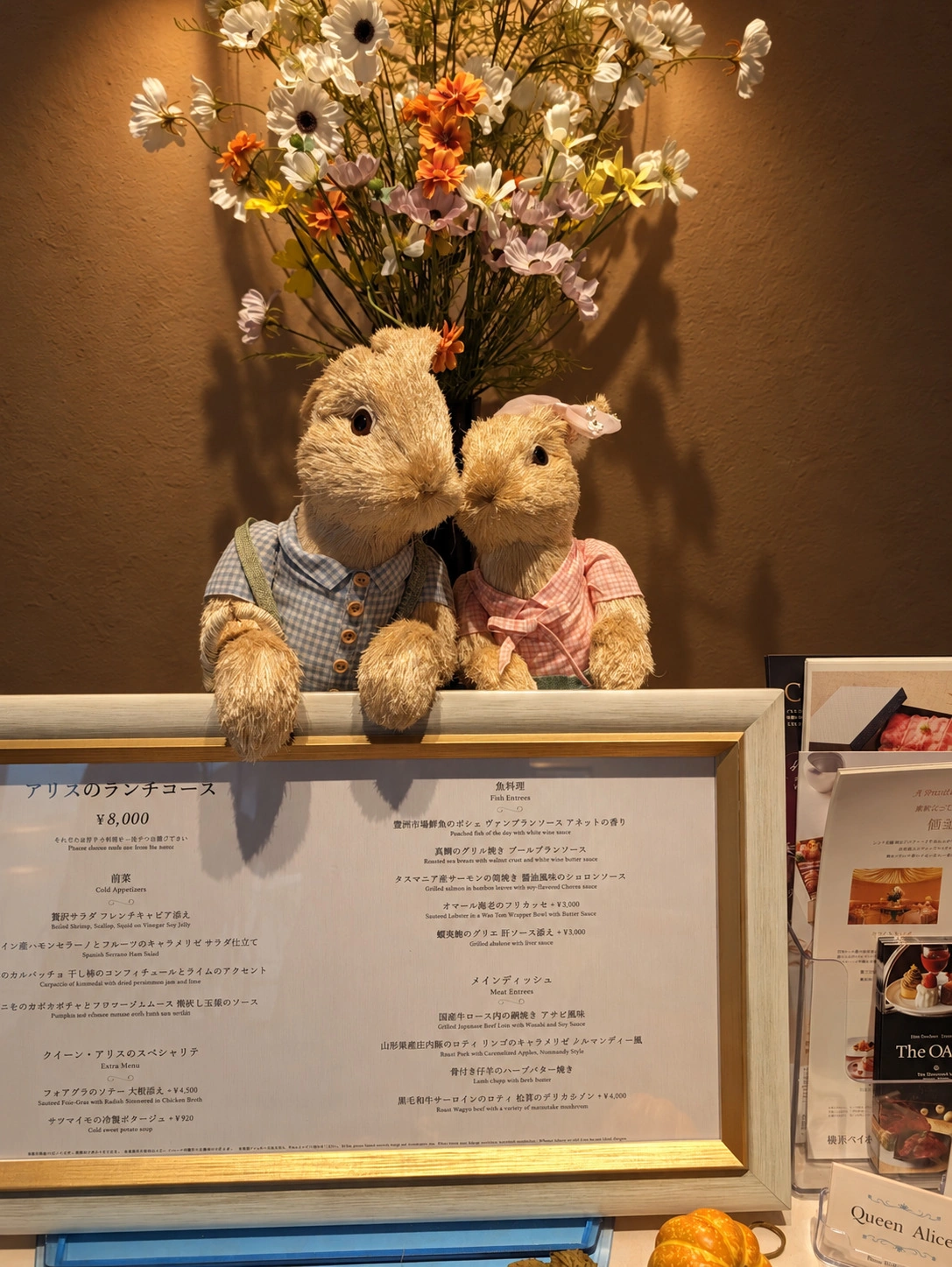 花とウサギの飾りが並ぶクイーン・アリスの店頭とランチメニュー(背景などはAIで加工)