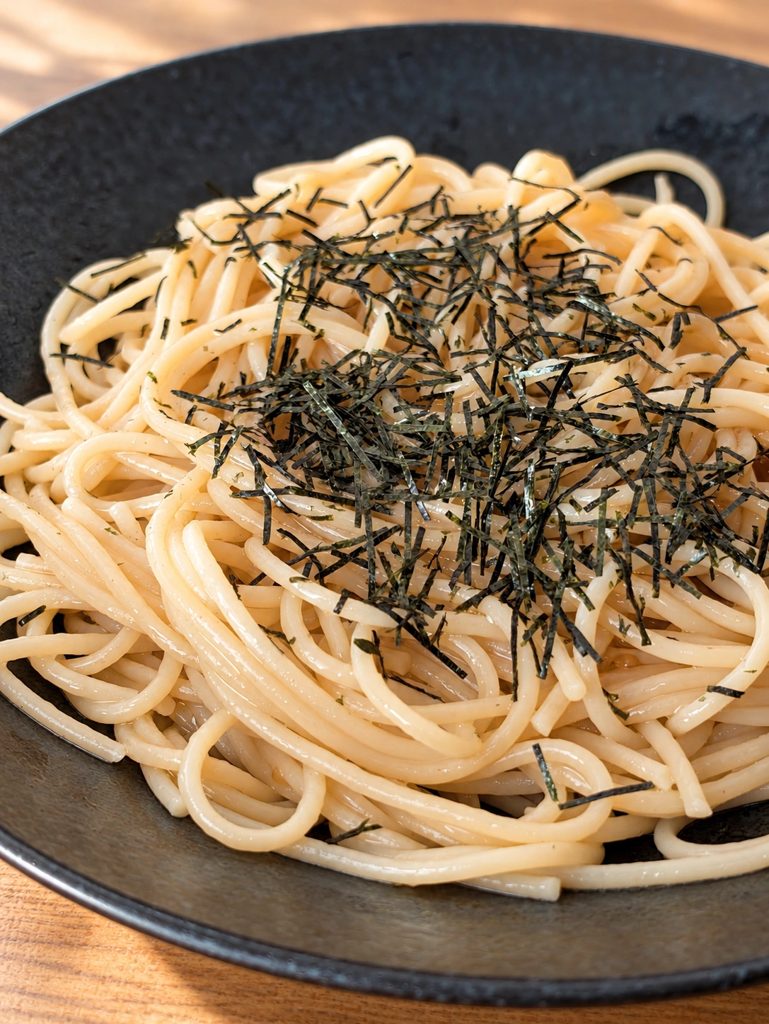 黒い皿に盛った海苔のせ明太パスタ(卓上などはAIで加工)